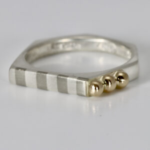 A striped sterling silver ring with three gold balls. the ring has six sides with the stripe across the tip of the ring.