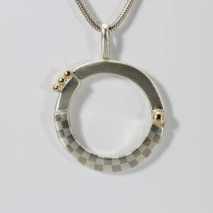 A round sterling silver pendant with a subtle checkerboard pattern and 14k gold ball. The Pendant is 1 1/2" x 1 1/8".