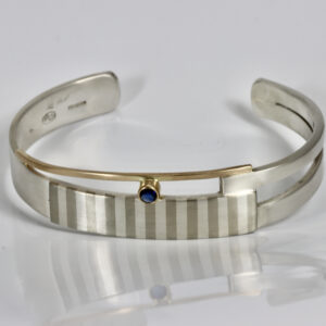 Striped cuff bracelet with a sapphire made of sterling silver and 14k gold.