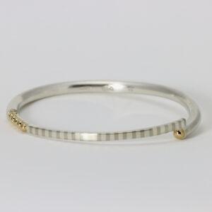 A sterling silver bangle with stripes and 14k gold balls.