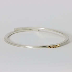 Sterling silver bangle with five solid 14k gold balls that are offset.