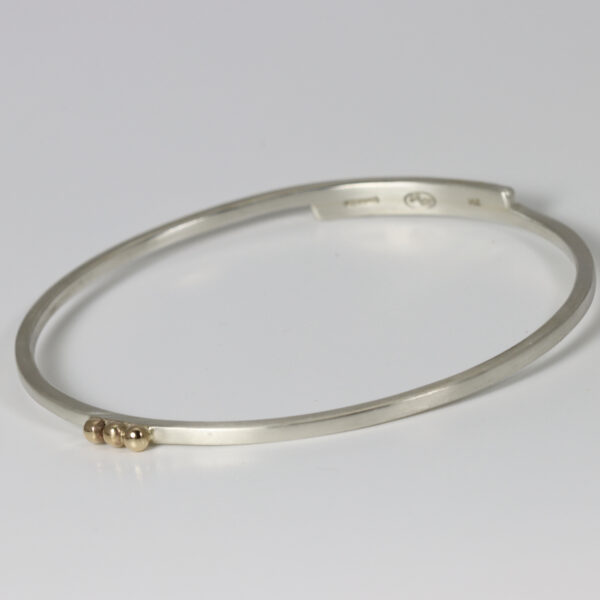 Oval shaped sterling silver bangle with three offset solid 14k gold balls.