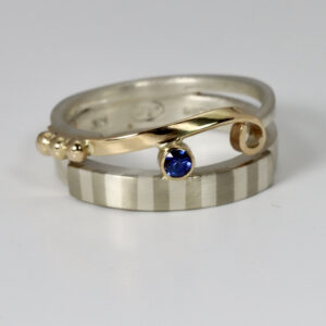 Mixed metal Ring with a sapphire and striped pattern.