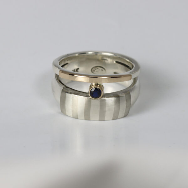Double band mixed-metal ring with a subtle striped pattern and a sapphire. Hand fabricated in sterling silver and 14k gold.