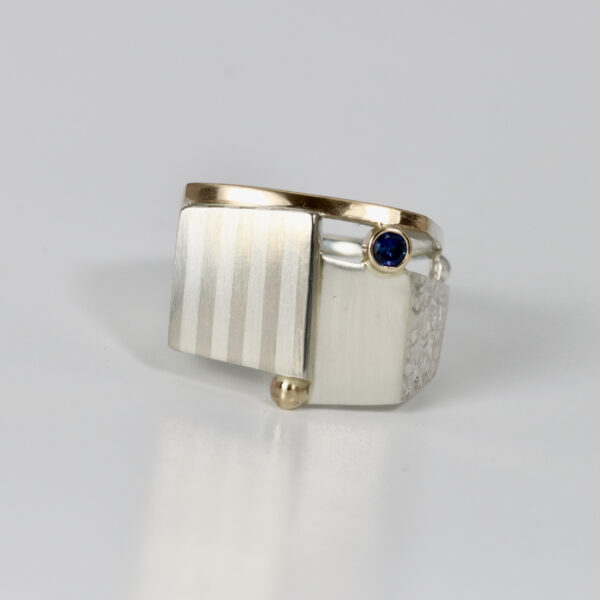 Contemporary mixed metals ring with a subtle striped pattern and a sapphire.