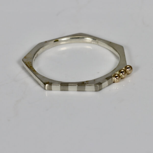 Narrow heptagon shaped ring with a subtle striped pattern and three 14k gold balls.