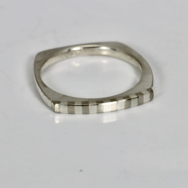 Striped stacking ring fabricated in sterling silver. The ring is squarish in shape and has a subtle striped pattern.