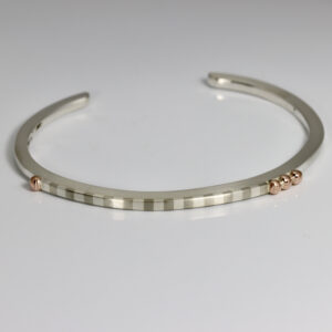 A Narrow cuff with a striped pattern and rose gold balls.