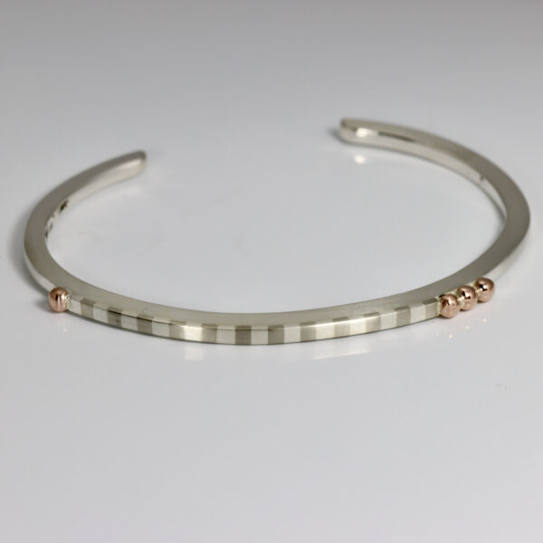 A Narrow cuff with a striped pattern and rose gold balls.