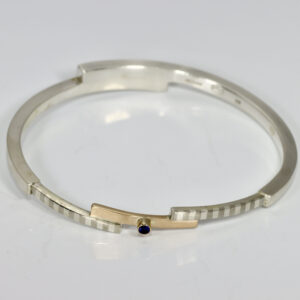 Mixed metal bangle bracelet with a striped pattern and a Sapphire.