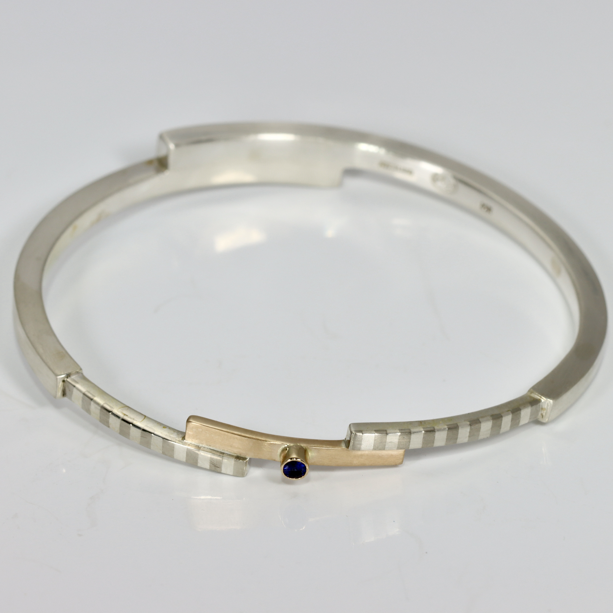 Mixed metal bangle bracelet with a striped pattern and a Sapphire.