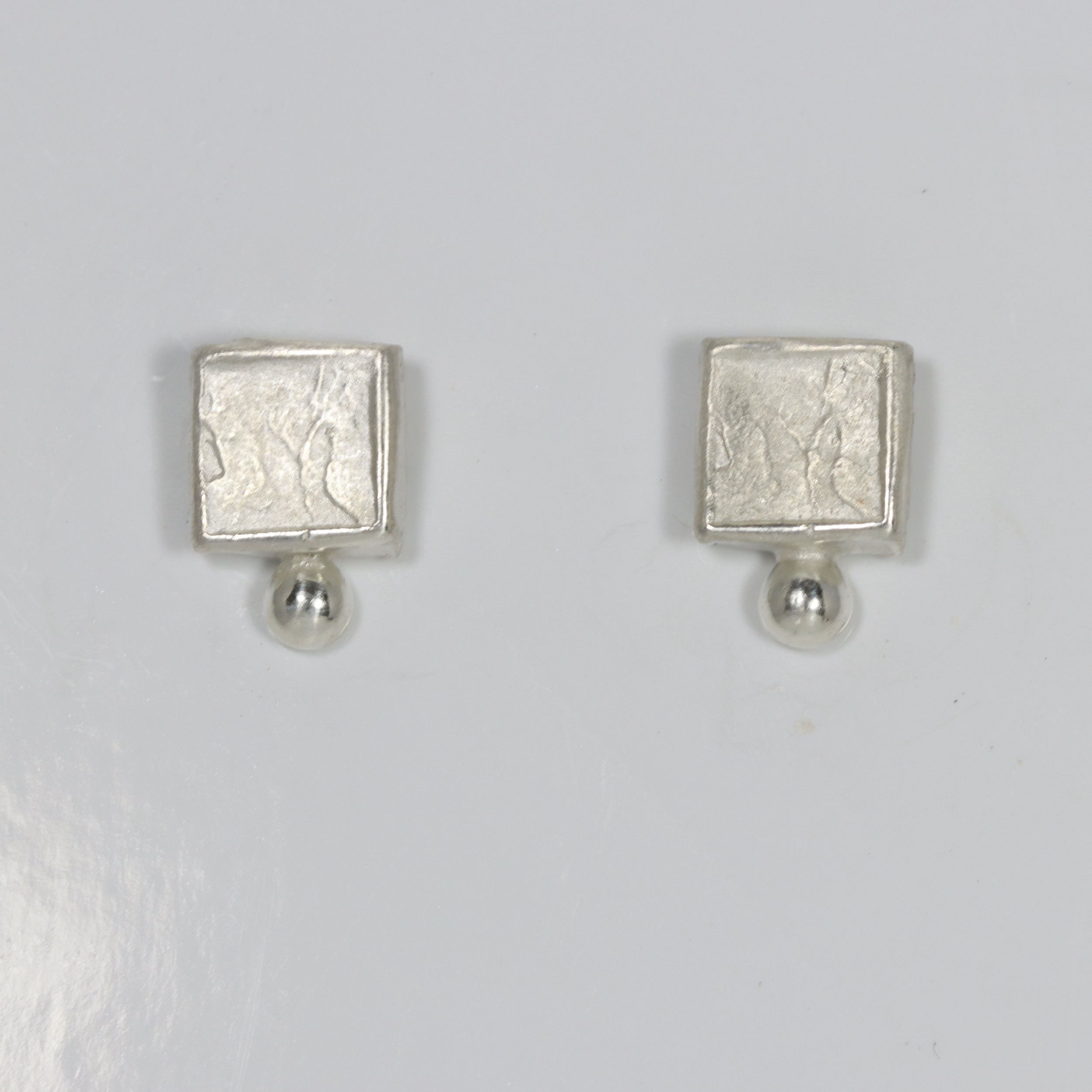 Sterling silver textured square with a smooth sterling ball at the bottom of the earring.