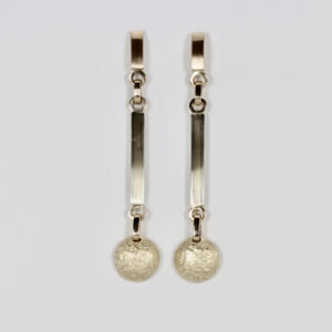A pair of long, multi-tiered 14k gold dangles. The earrings feature a top post that secures to the ear, holding a middle section made of a long, narrow drop component with an alternating pattern of 14k yellow gold and white gold stripes. Suspended from the bottom of this slender bar is a domed circle with a textured finish.