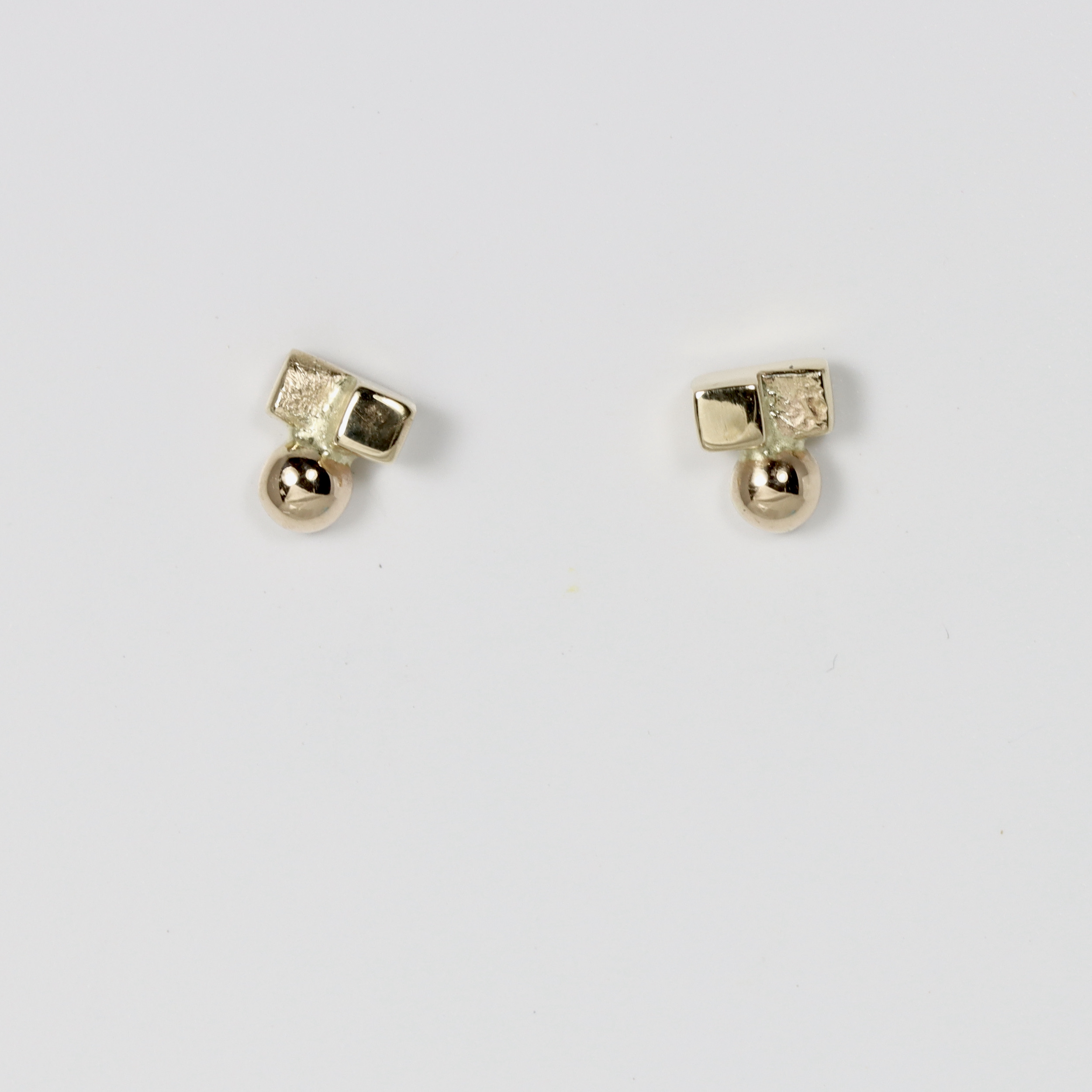 A modern minimalist 14k gold stud earrings. The stud features a tiny flat square shape and a textured square shape seamlessly paired with a miniature round gold ball bead.