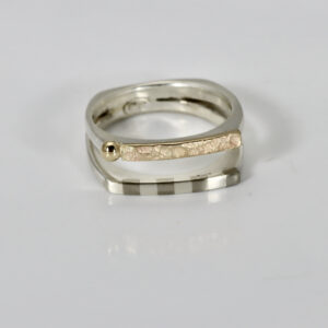 Two connected sterling silver rings worn together as a double band, showing a detailed striped pattern on one band and an organic texture with a ball on the other band.