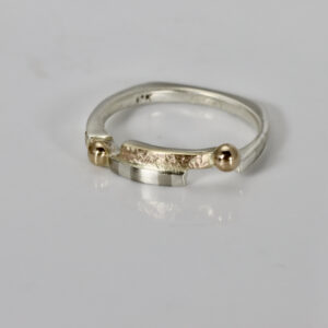 A narrow offset sterling silver and gold band ring featuring an organic 14k texture, a subtle striped pattern, and 14k gold balls.