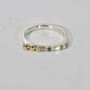 A narrow square-shaped sterling silver ring featuring a subtle striped pattern and a cluster of three small 14k gold balls.