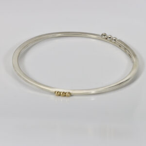 A matte sterling silver bangle bracelet featuring shiny 14k gold and silver decorative balls spaced across the band.