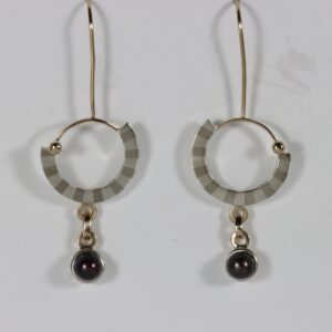 A striped circular earring with a dangling black pearl. Hand fabricated in sterling silver and 14k yellow gold.