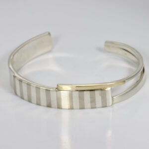 A wide subtly striped patterned cuff fabricated in sterling silver with 14k accent.