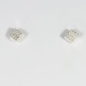 The miniature three-dimensional cube features smooth, polished sides, while its top outward-facing surface is detailed with a distinct texture create by a lost wax casting technique.