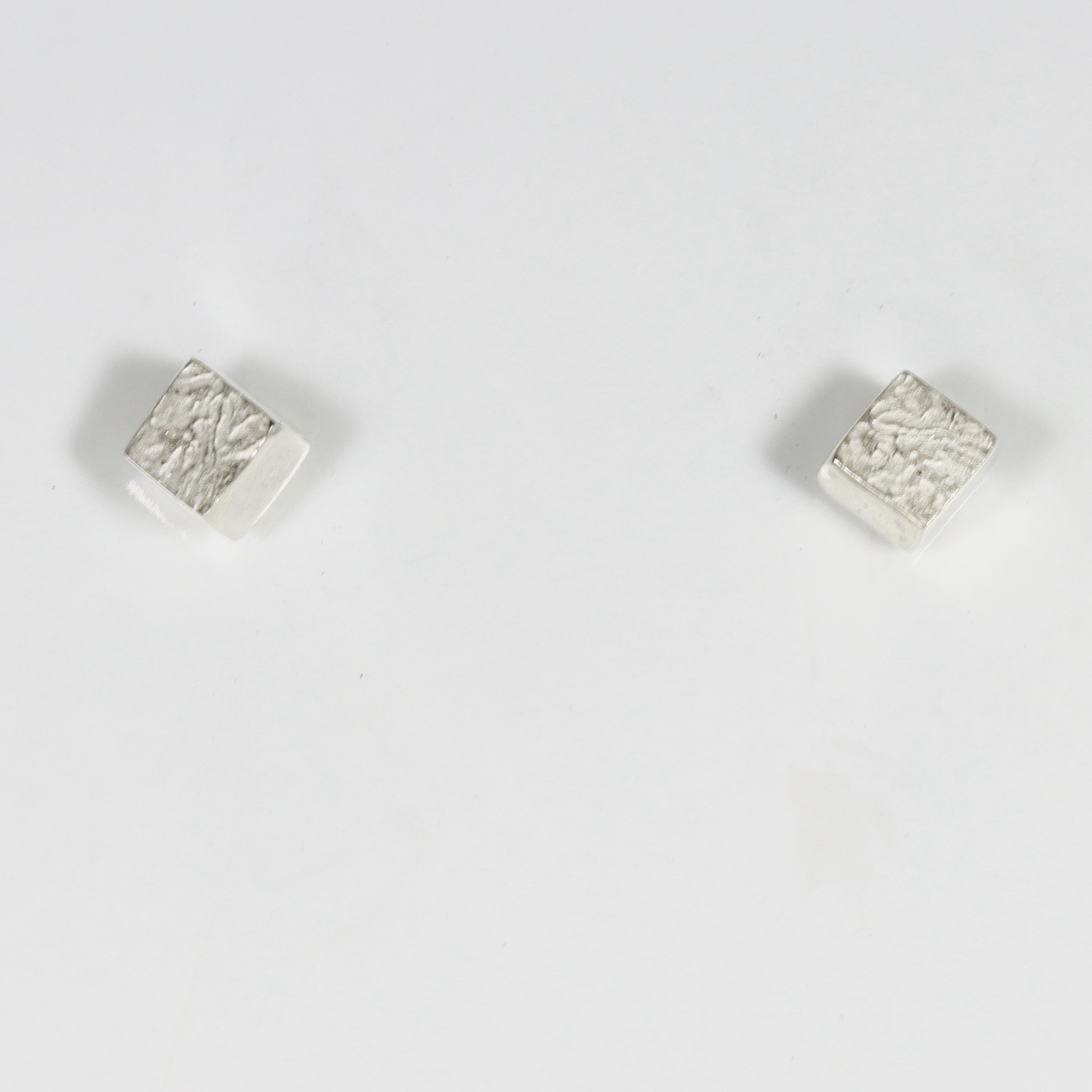 The miniature three-dimensional cube features smooth, polished sides, while its top outward-facing surface is detailed with a distinct texture create by a lost wax casting technique.