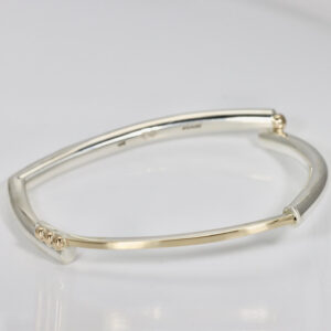 Gold and sterling silver bangle. The bracelet is squarish in shape. Across the top of the bangle is gold over sterling. There are solid 14k gold ball accent adding interest at every angle.