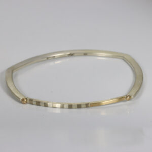 Narrow minimalist bangle bracelet featuring marriage of metals striped pattern, contrasted against polished 14k yellow.