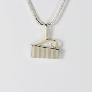 Close-up of a striped silver pendant highlighted by an elegant, polished 14k yellow gold French curve accent piece.