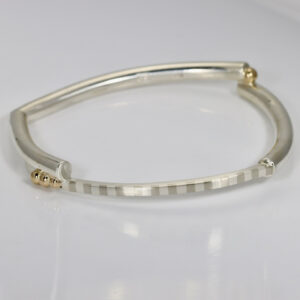 Modern squarish bangle bracelet featuring a hand-fabricated striped pattern in sterling silver, accented by solid 14k gold balls along the surface.